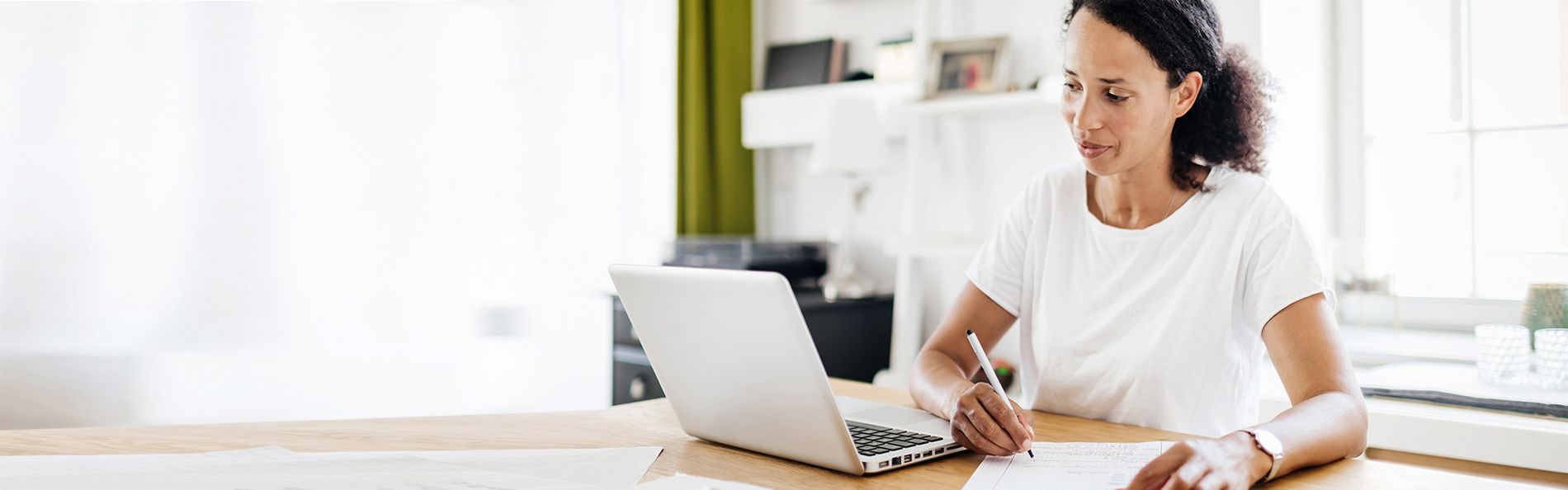 Frau sitzt vor Laptop und macht sich Notizen