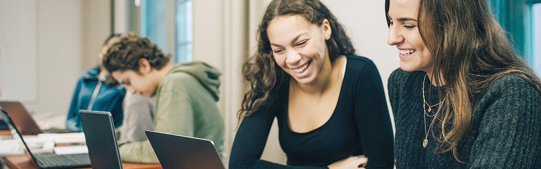 Zwei Schülerinnen sitzen am Laptop und lachen