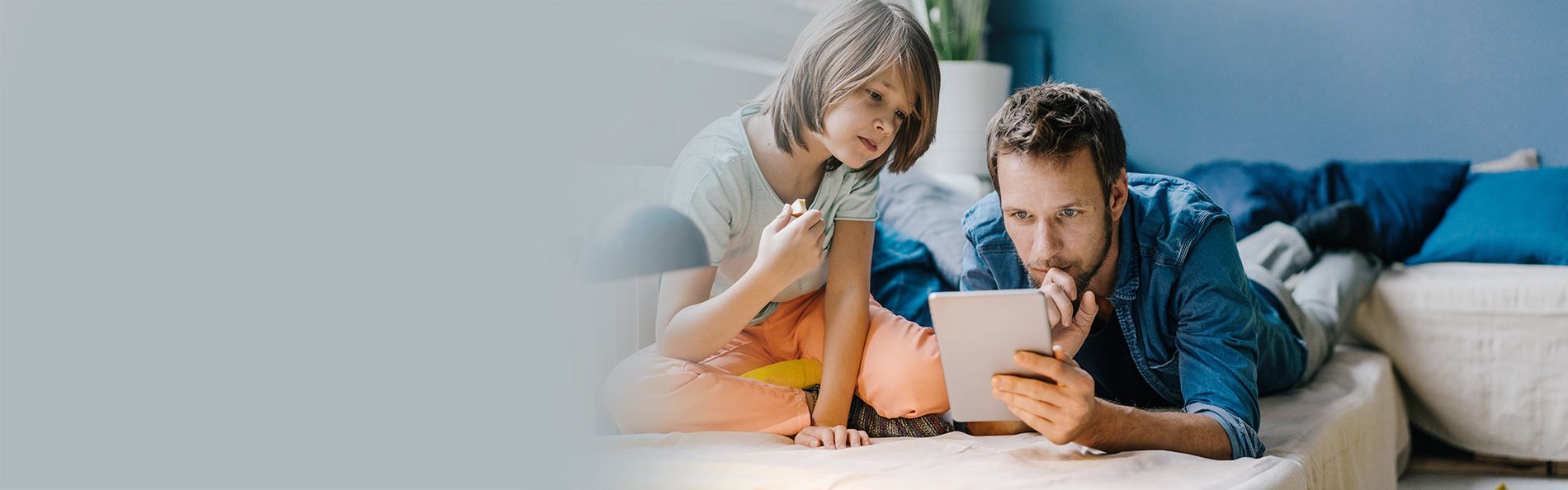 Vater und Sohn liegen auf der Couch und schauen in ein Tablett