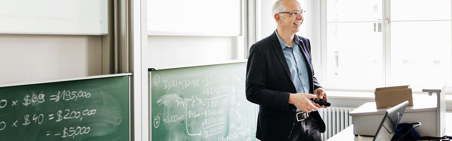 Professor lacht und steht vor Tafel in Lehrsaal