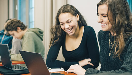 Zwei Schülerinnen sitzen am Laptop und lachen