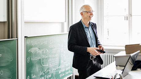 Professor lacht und steht vor Tafel in Lehrsaal