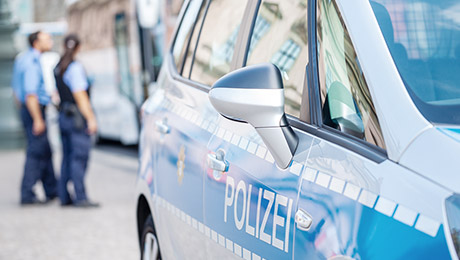 Polizeiauto mit Polizisten im Hintergrund