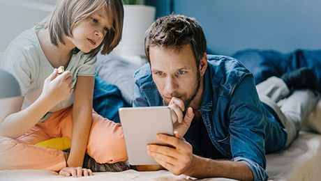 Vater und Sohn liegen auf der Couch und schauen in ein Tablett